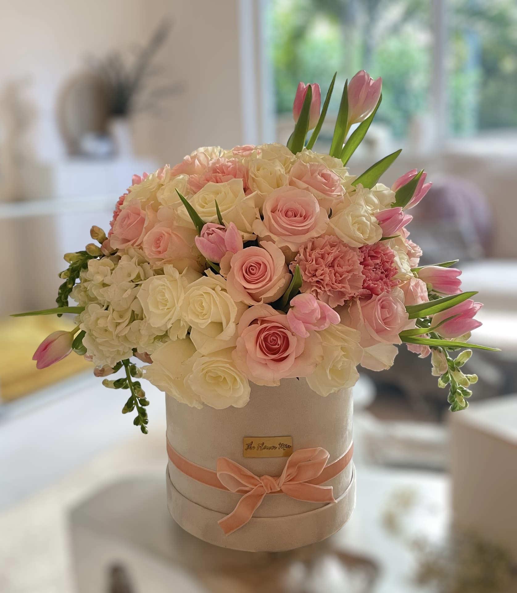 Blush Garden - Blush pink and ivory roses with white hydrangeas, carnations and airy tulips in a pale round hatbox, tied with peach satin ribbon-romantic gift for anniversaries or Mother's Day.
