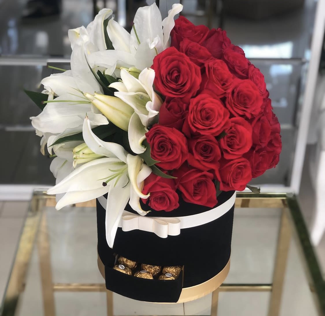 Midnight Romance - Red roses and white lilies in a black hatbox with white ribbon and gold trim, finished with a front pocket of chocolates-bold, romantic gift-ready arrangement.