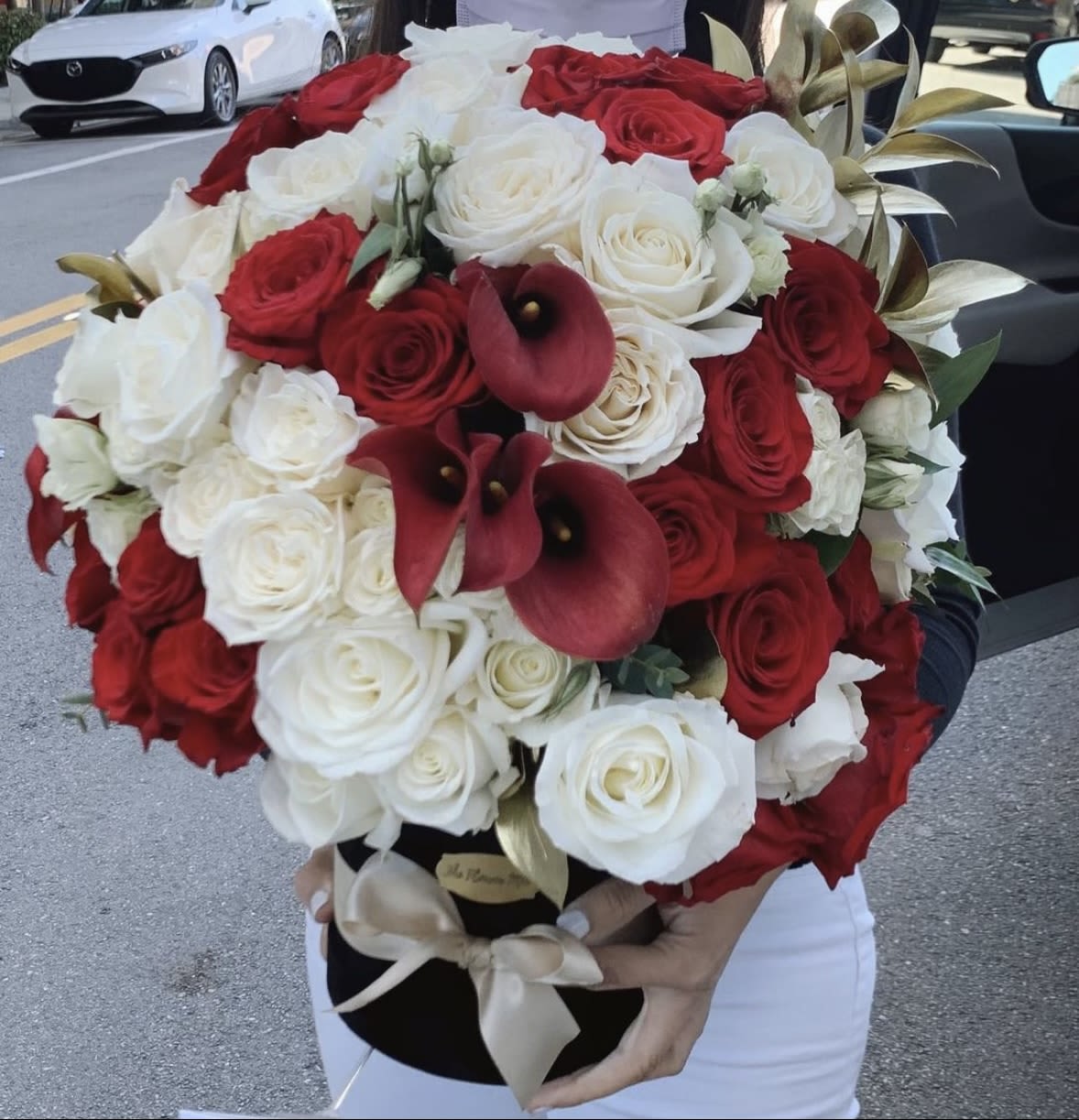 Red and Gold Box - Red and white roses with burgundy calla lilies in a black hatbox, tied with a pale satin ribbon-lush, dramatic, and romantic for anniversaries, weddings, or special moments.