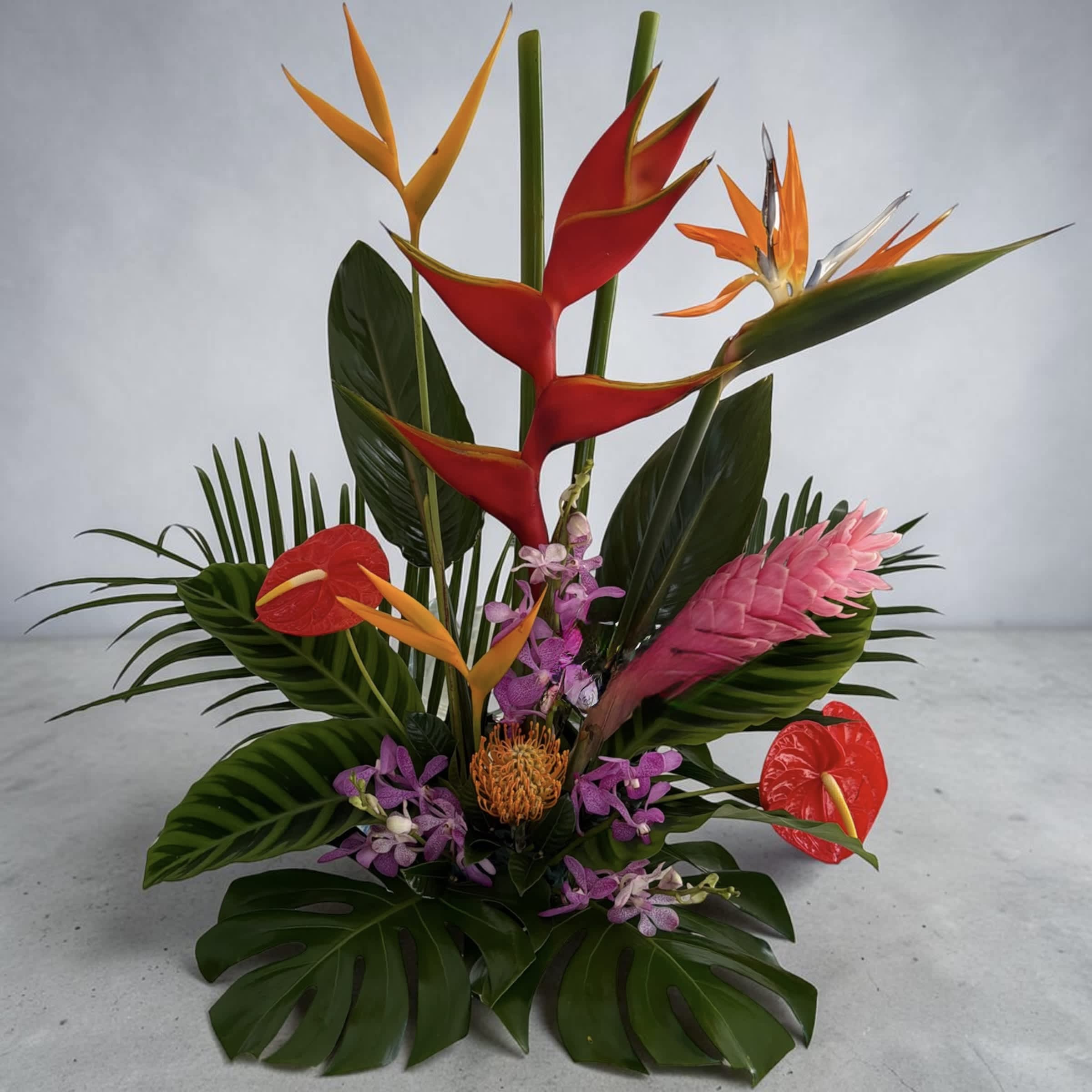 Tropical arrangement with red and orange heliconia, pink ginger, and purple orchids