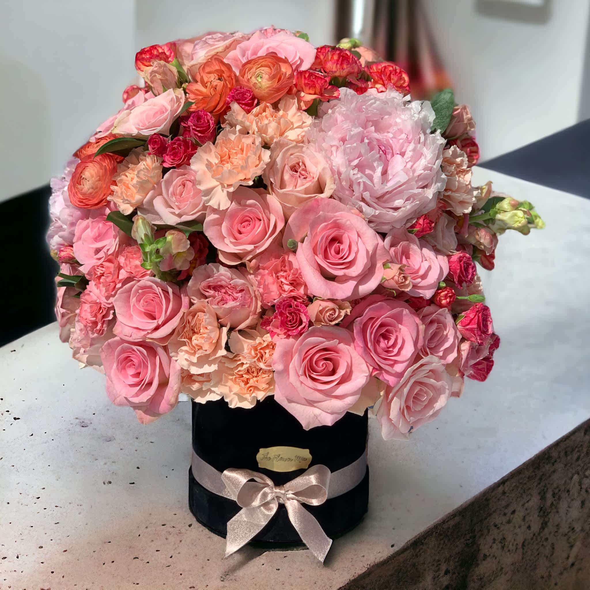 Pink and peach roses arranged in a black hat box with a ribbon