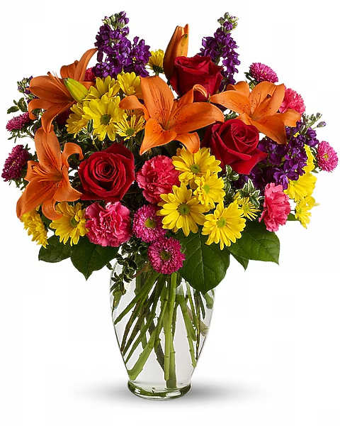 Bouquet of orange lilies, red roses, and yellow daisies in a clear glass vase