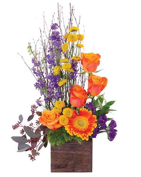 Orange roses and a gerbera daisy in a wooden box with purple and yellow flowers