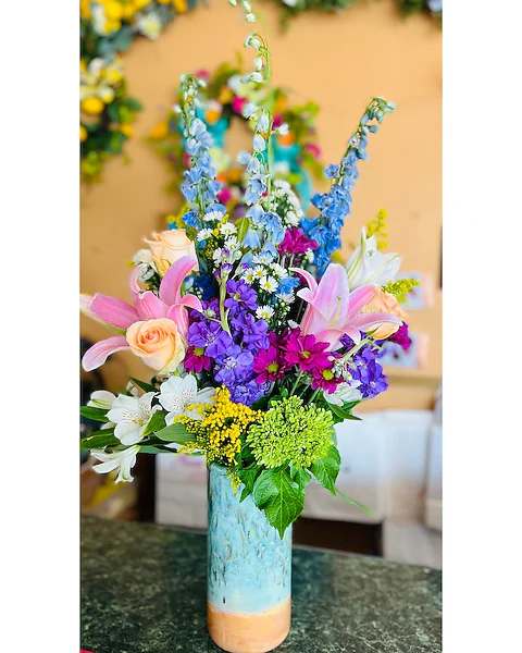 Tall mixed bouquet in a blue ceramic vase with pink lilies and purple flowers