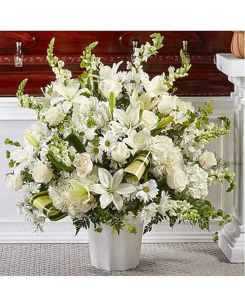 White floral arrangement in a white vase with lilies and daisies