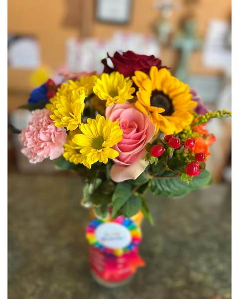 Mixed bouquet with sunflowers, roses, and pink carnations in a glass vase