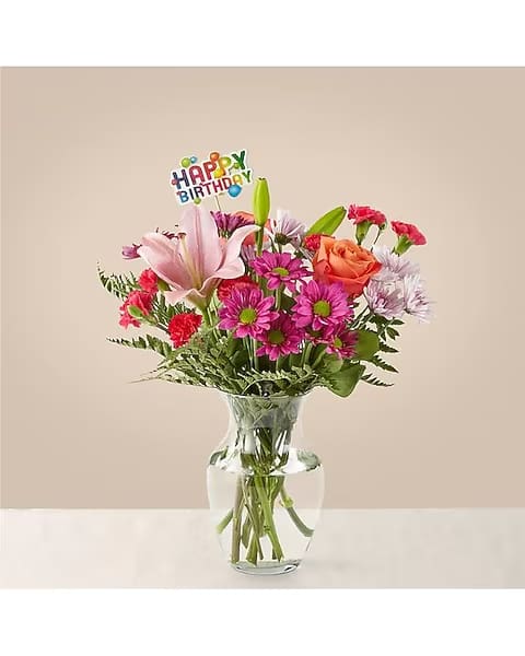 Mixed bouquet in a clear glass vase with a birthday pick