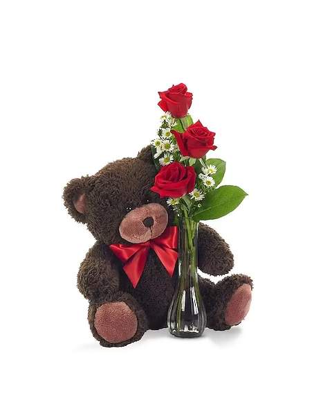 Teddy bear holding red roses in a glass vase