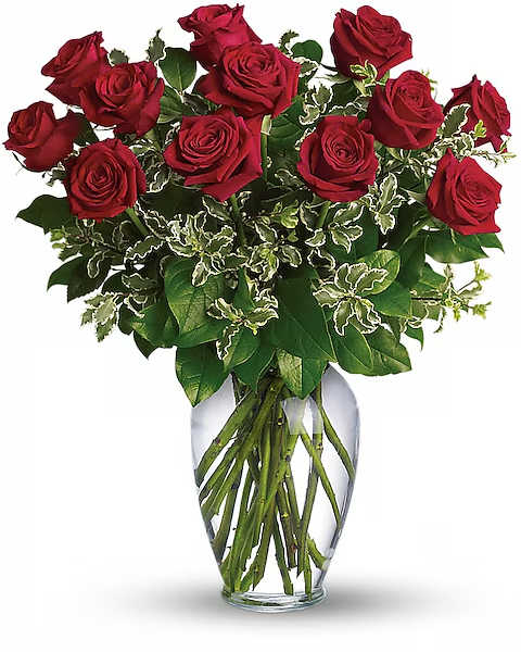 Red roses arranged in a clear glass vase with variegated greenery
