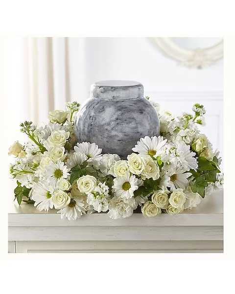 White daisies and cream roses arranged around a gray urn
