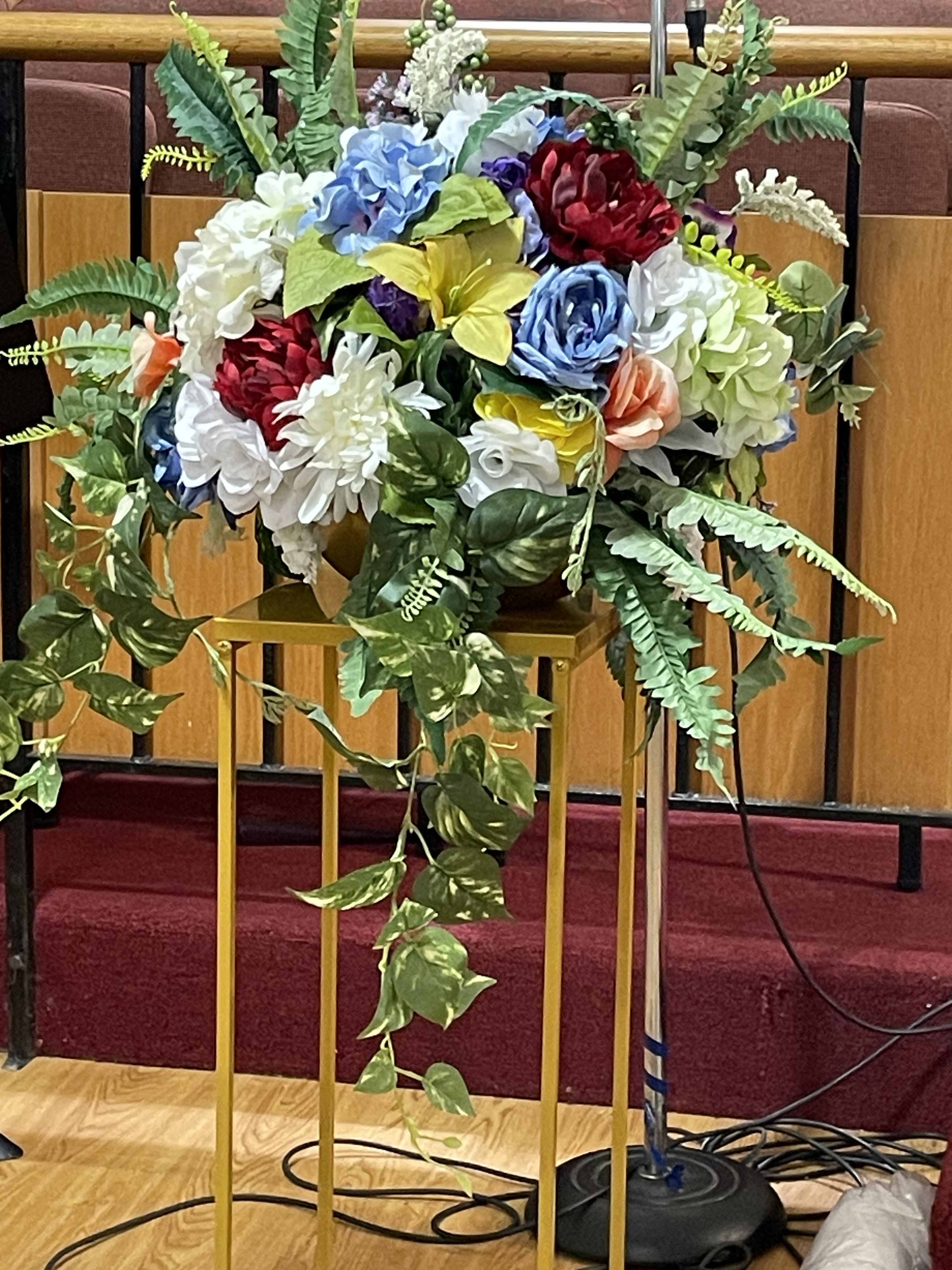 Large floral arrangement with multicolored blooms and trailing greenery on a stand