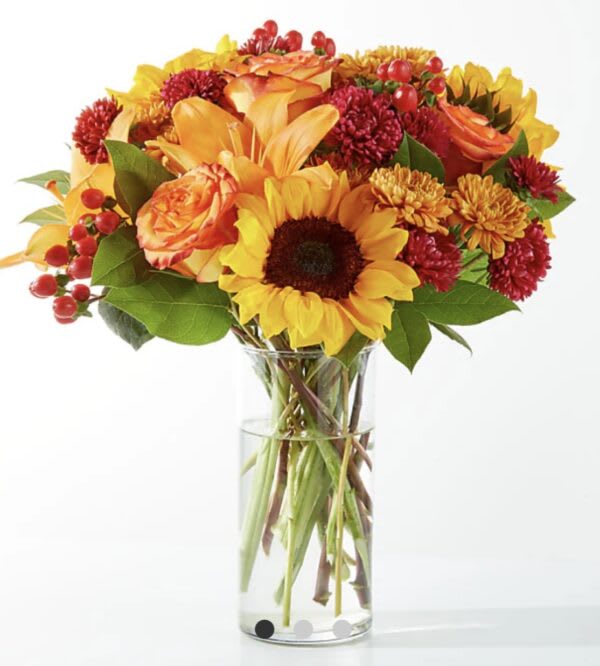 Bouquet of sunflowers, roses, and mums in a clear glass vase