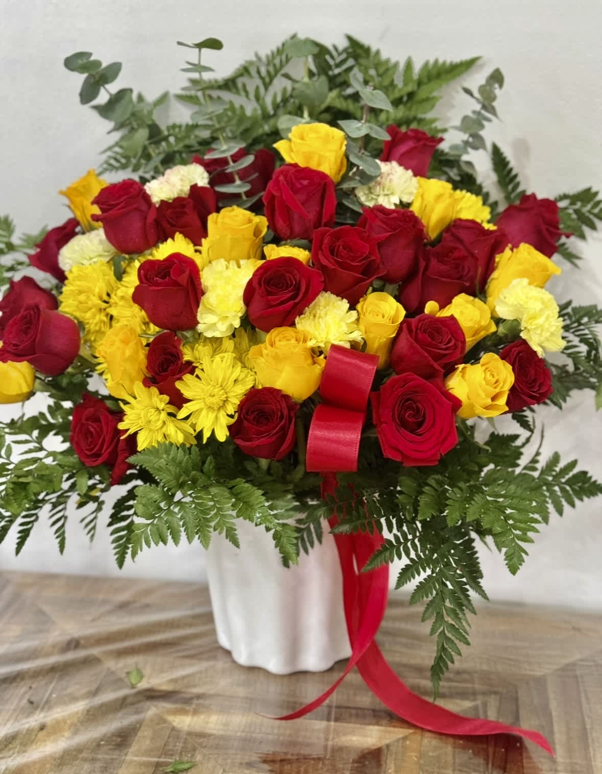 Bouquet of red and yellow roses with yellow chrysanthemums in a white vase