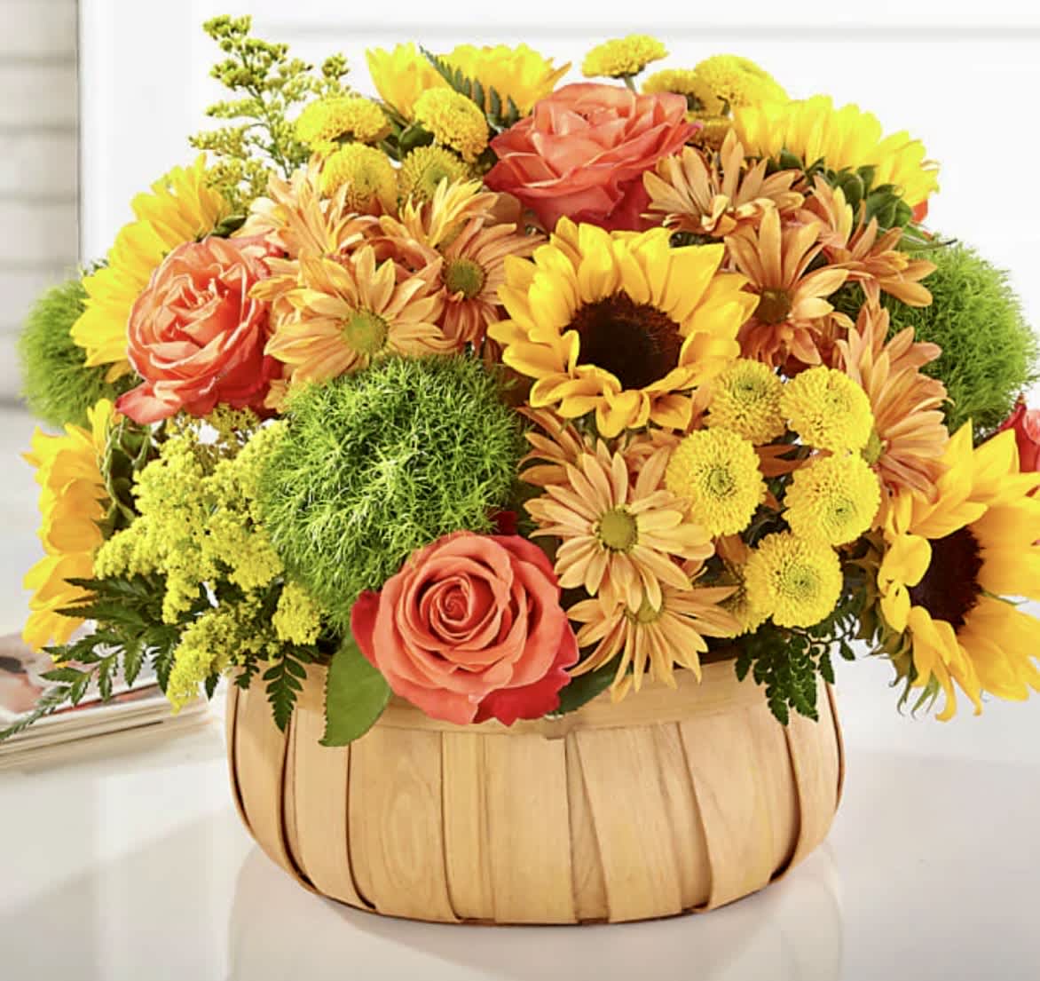 Basket arrangement of yellow sunflowers, coral roses, and orange daisies