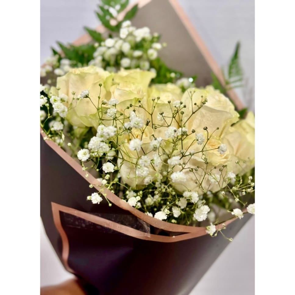 Bouquet of pale yellow roses with white baby's breath in dark wrapping