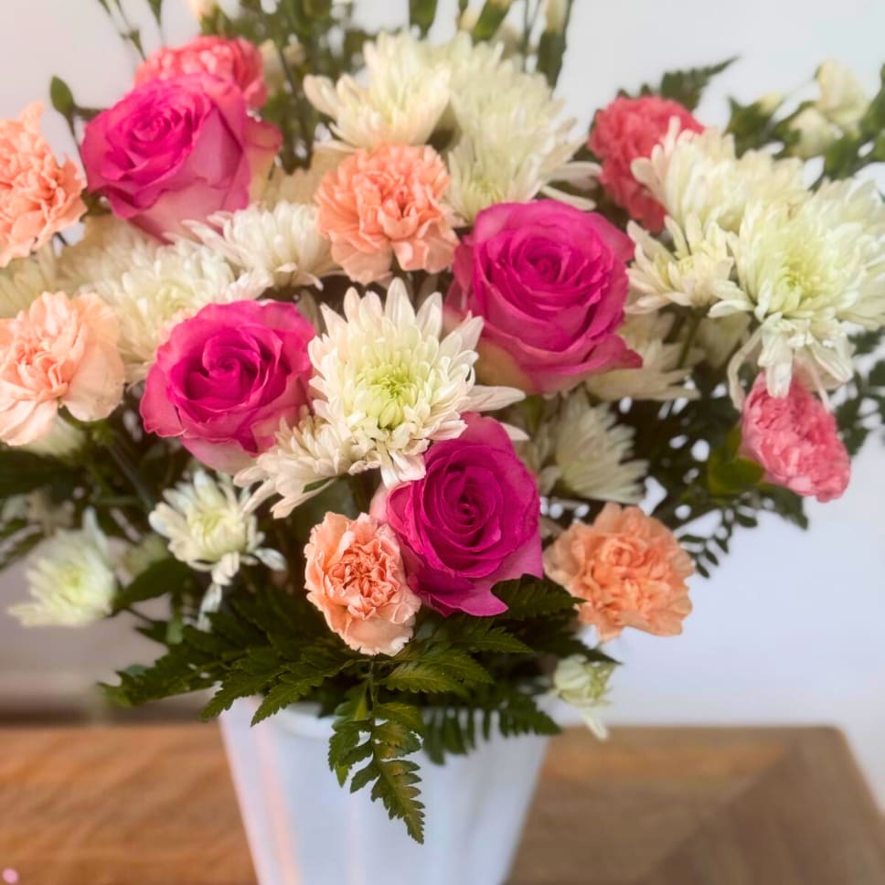 Pink roses, white chrysanthemums, and peach carnations in a white vase