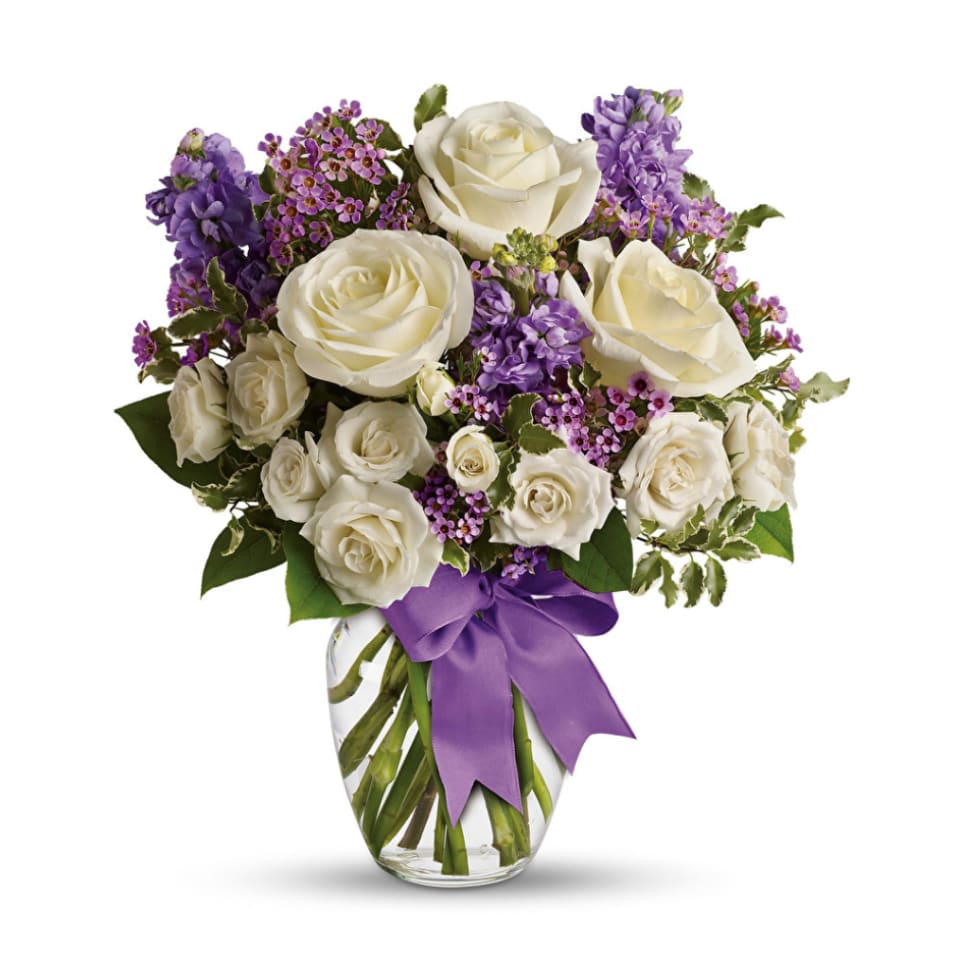 White roses and purple flowers in a clear glass vase with a purple ribbon
