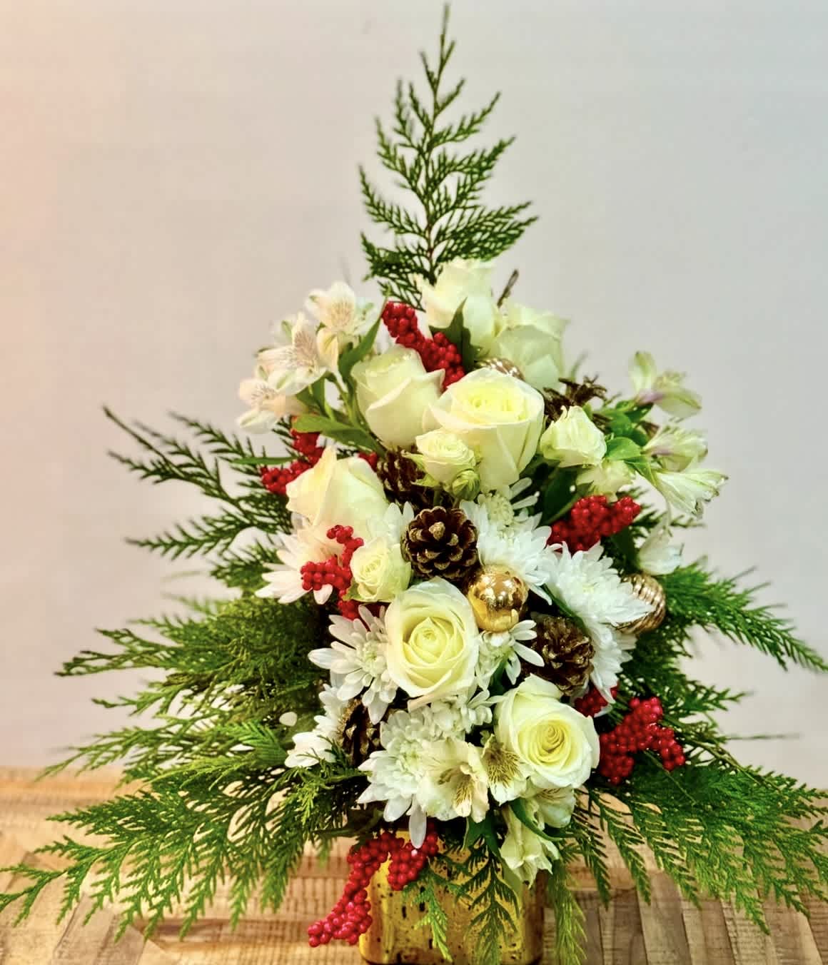 White roses and daisies arranged with red berries in a gold vase