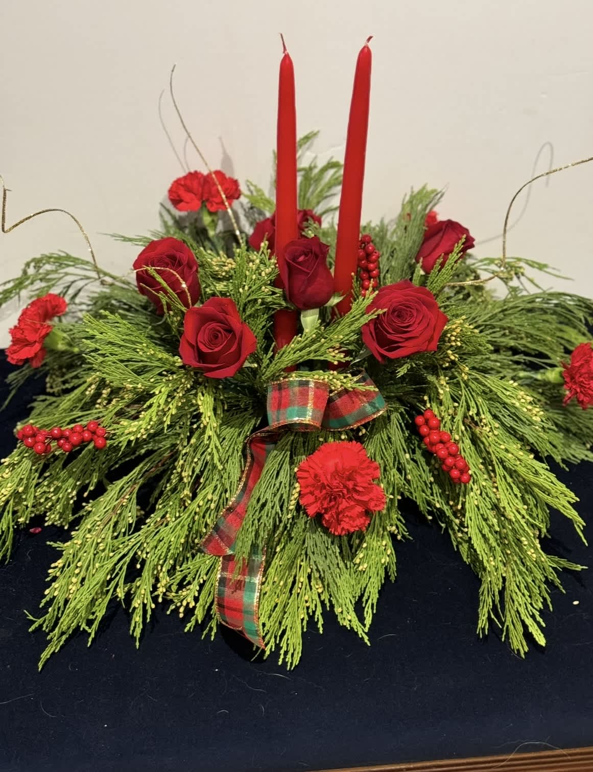 Red roses and carnations arranged with candles and plaid ribbon.