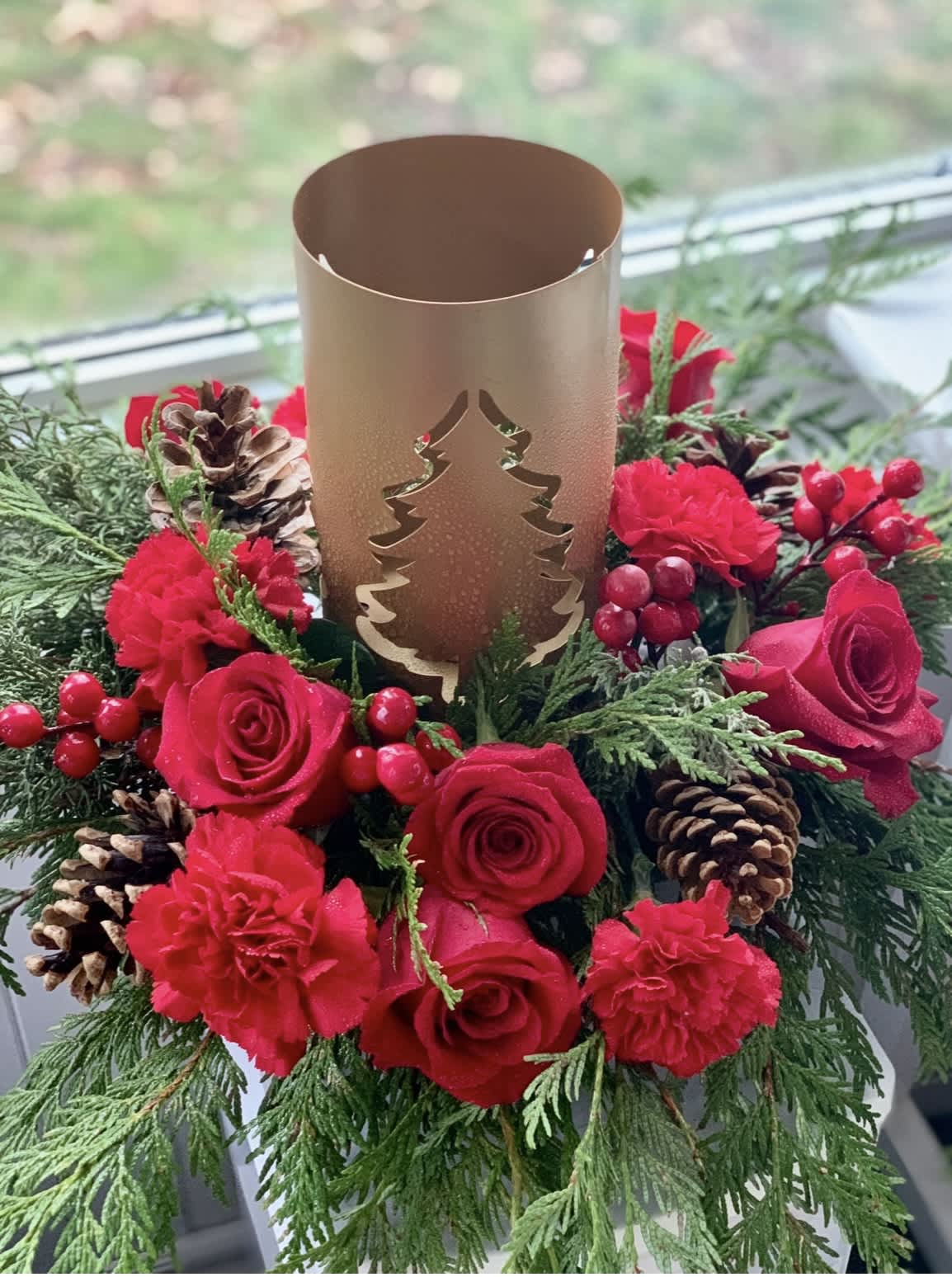 Red roses and carnations arranged around a gold candle holder with pinecones.