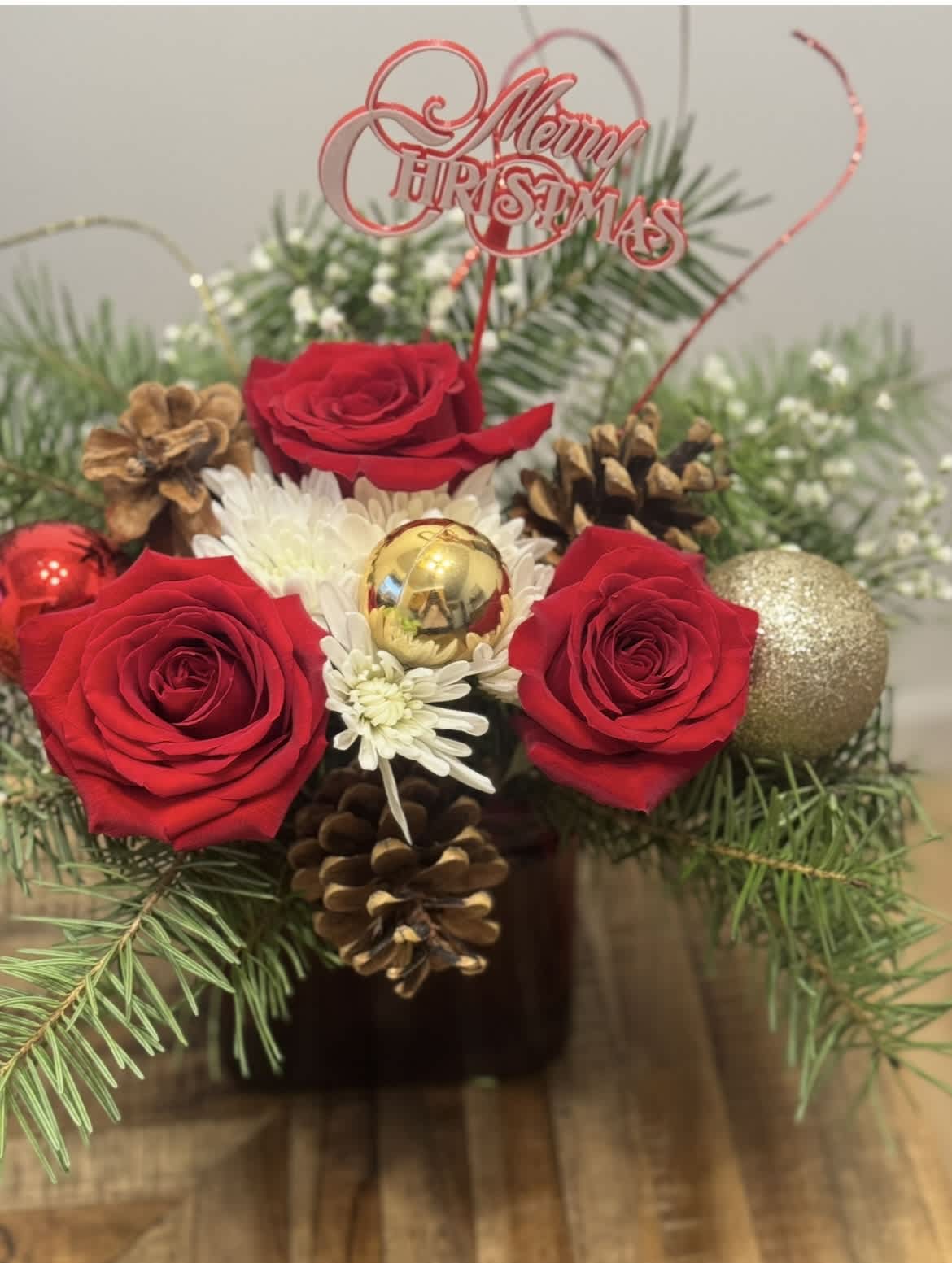 Christmas arrangement with red roses, white daisies, pinecones, and ornaments