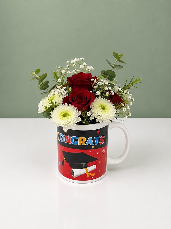 Congrats Cup Arrangement - Bright red roses paired with crisp white daisy-like blooms create an instantly celebratory look in this Congrats Cup arrangement—perfect as a graduation bouquet or a cheerful "congrats" gift. The white ceramic mug, printed with a colorful CONGRATS design, makes the presentation feel personal and festive; the strong red-and-white contrast reads joyful and confident, so the person you're honoring will feel seen and applauded.  Delicate white filler flowers and airy eucalyptus-like stems lift the composition, adding light texture and a fresh green accent that keeps the arrangement feeling modern and lively. Arranged compactly in the mug, this is an everyday gift-size floral piece—easy to display on a desk, kitchen counter, or dorm room shelf. The sturdy ceramic mug also offers a keepsake your recipient can reuse long after the blooms fade.  Give this to a new graduate, a coworker celebrating a milestone, or anyone who deserves a small, happy surprise—the kind of bouquet that makes someone feel truly celebrated. Care: keep blooms in fresh water, trim stems, and change the water every 2-3 days to extend vase life; the mug serves as a single-serving keepsake vessel, ideal for small spaces.  Please note: Flower colors and varieties may vary slightly based on seasonal availability. Any substitutions will be made with fresh flowers of equal or greater value while maintaining the overall style and beauty of the arrangement.