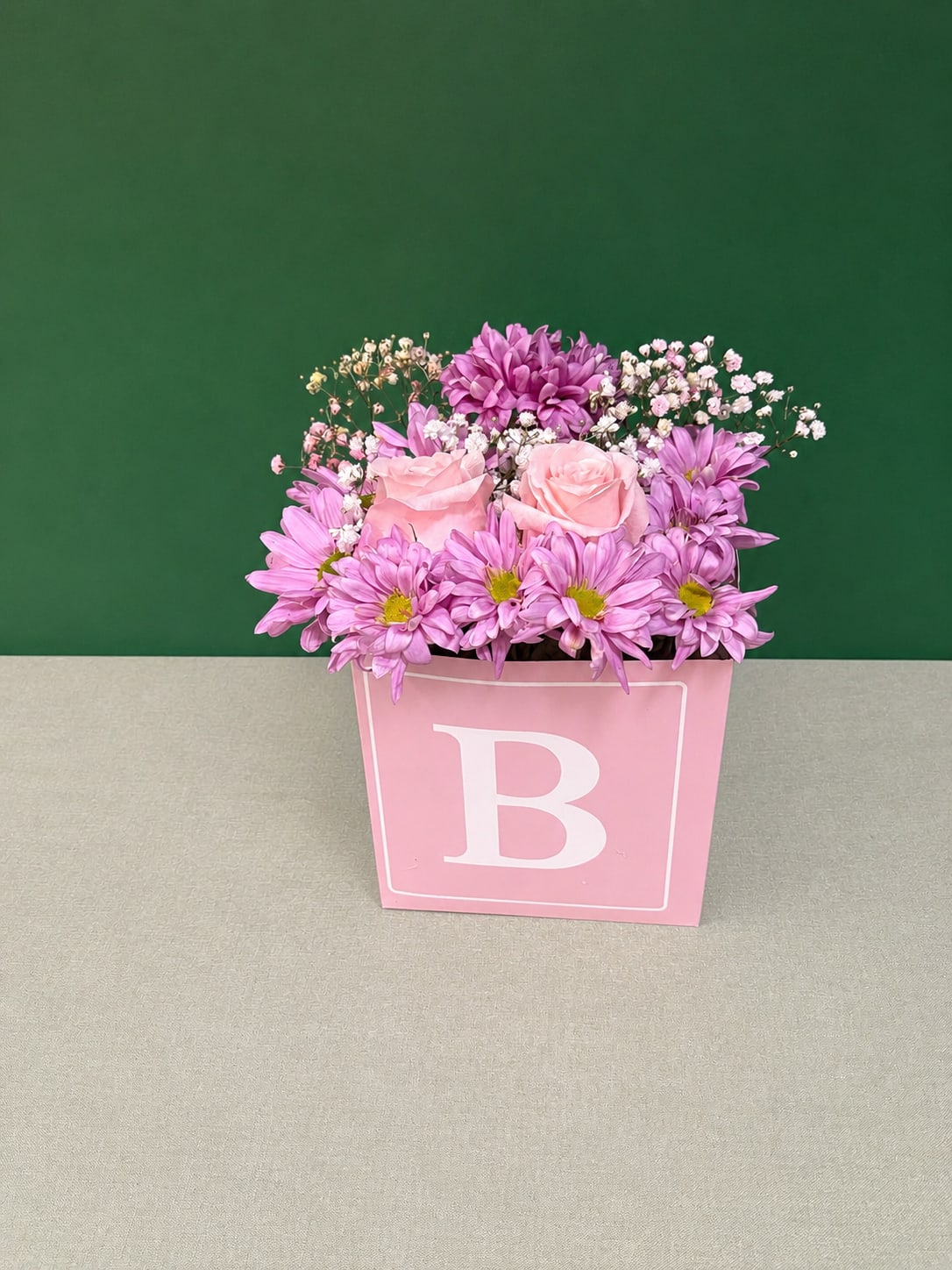 Pink and purple flowers arranged in a pink box with a large letter B