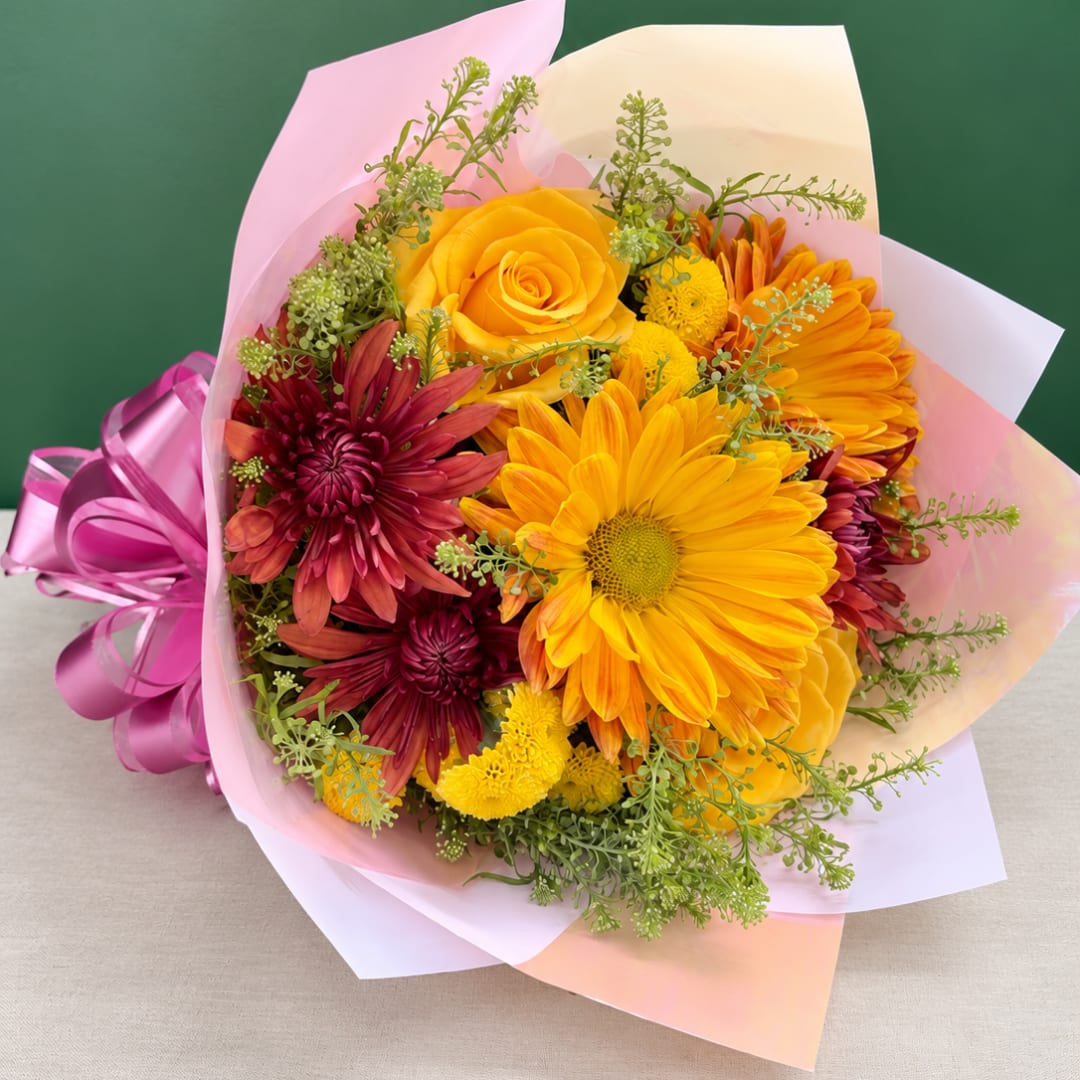 Bouquet of yellow and burgundy flowers wrapped in pink paper with a ribbon
