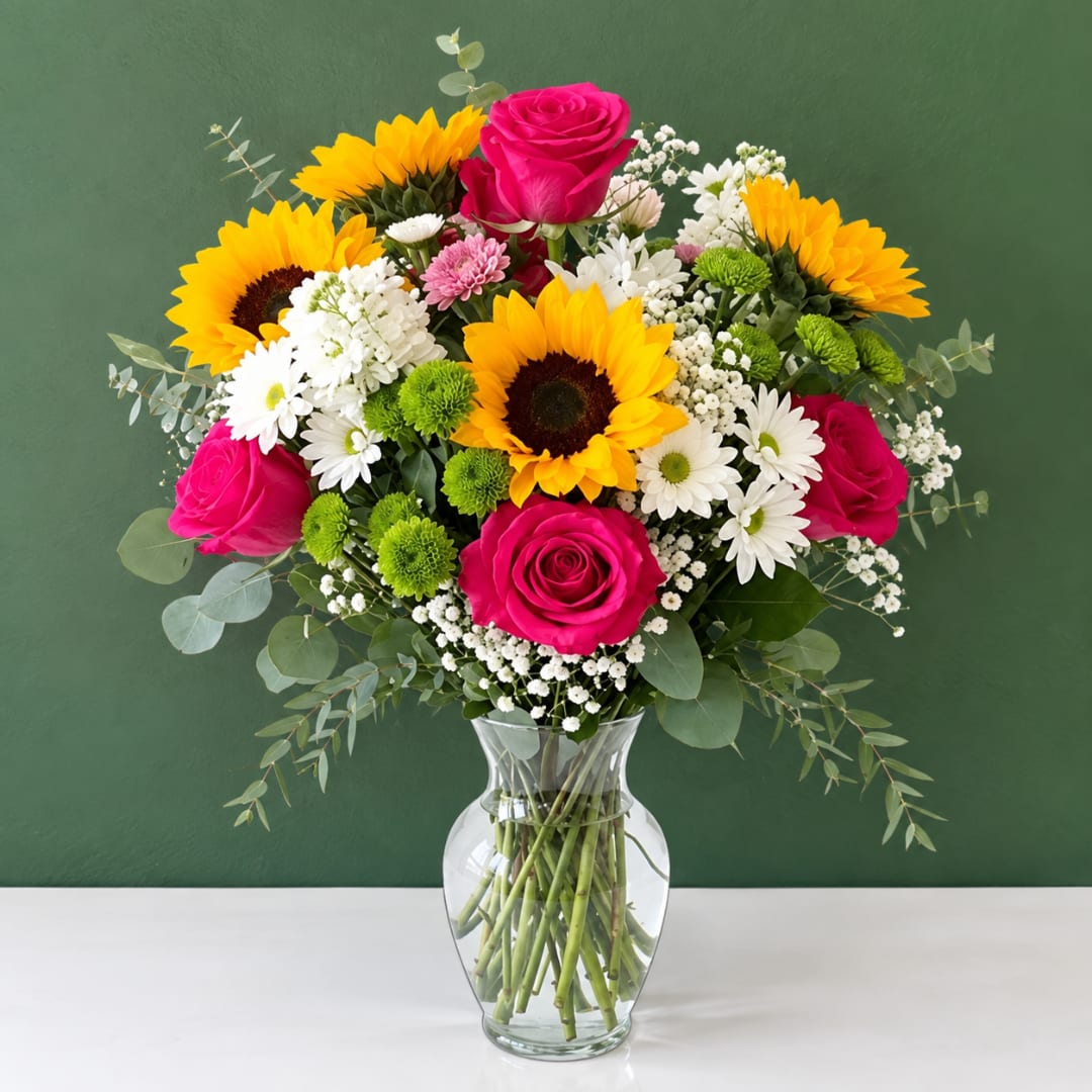 Bouquet of sunflowers, pink roses, and white daisies in a clear glass vase