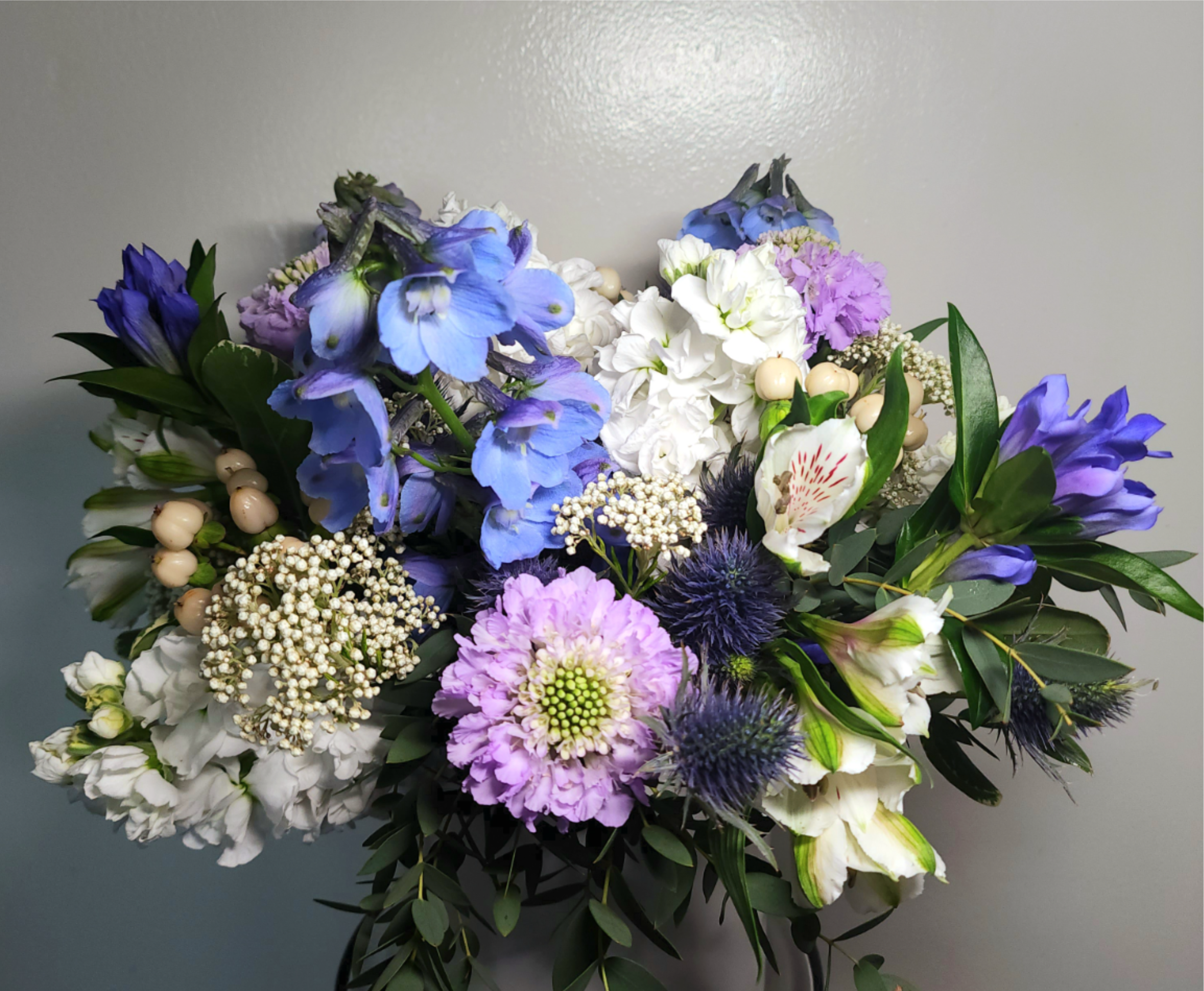 Bouquet of blue, white, and lavender flowers with dark greenery