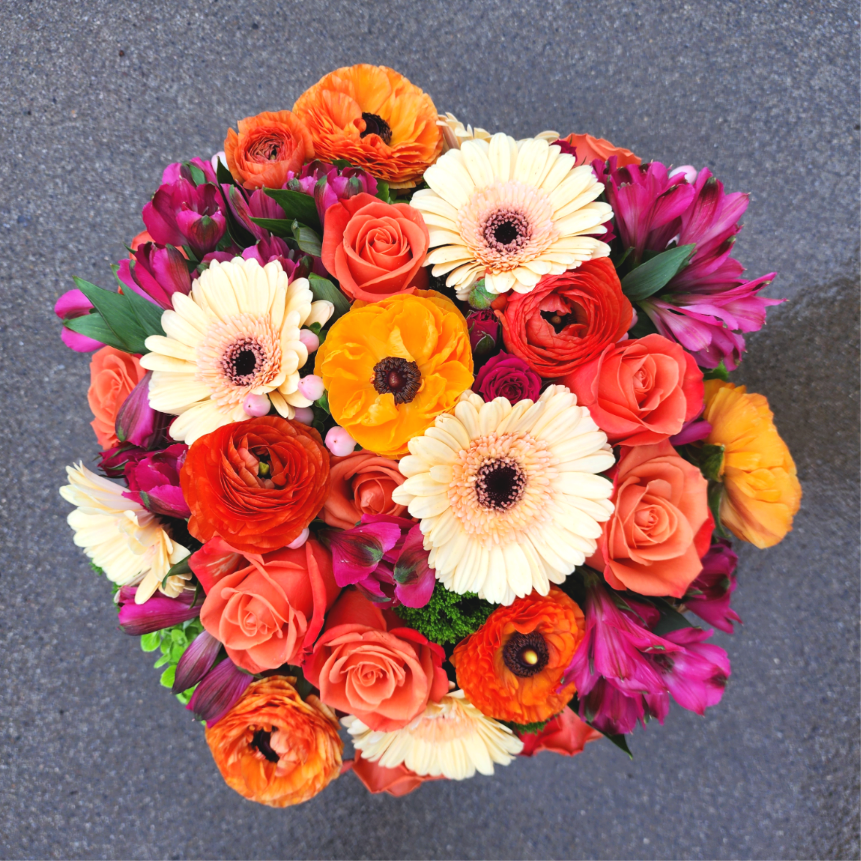 Round bouquet of orange, coral, cream, and magenta flowers