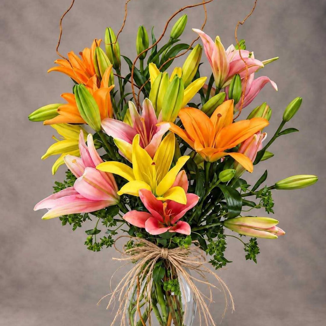 Bouquet of multicolored lilies in a clear vase with a raffia bow