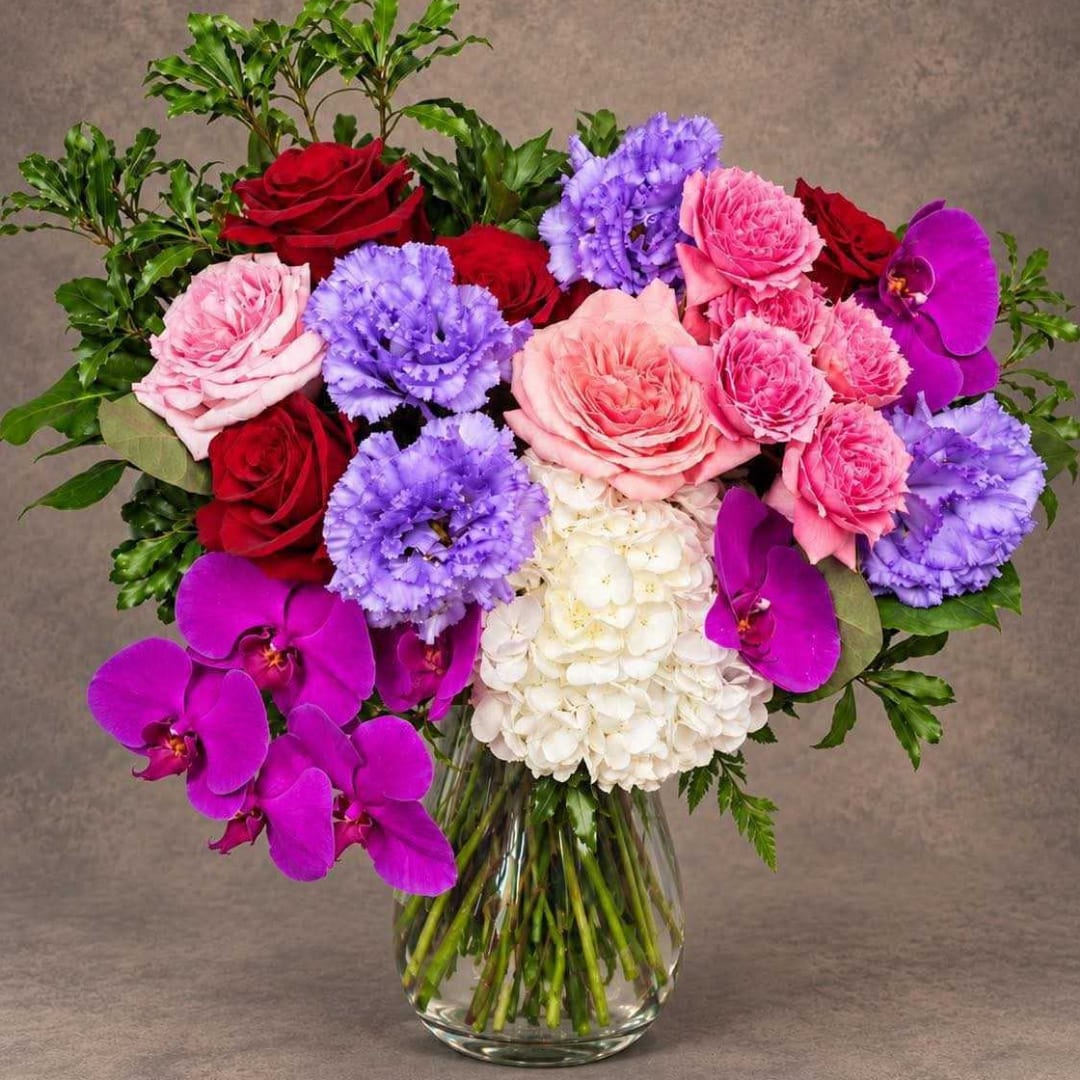 Mixed bouquet of roses, carnations, hydrangea, and orchids in a glass vase