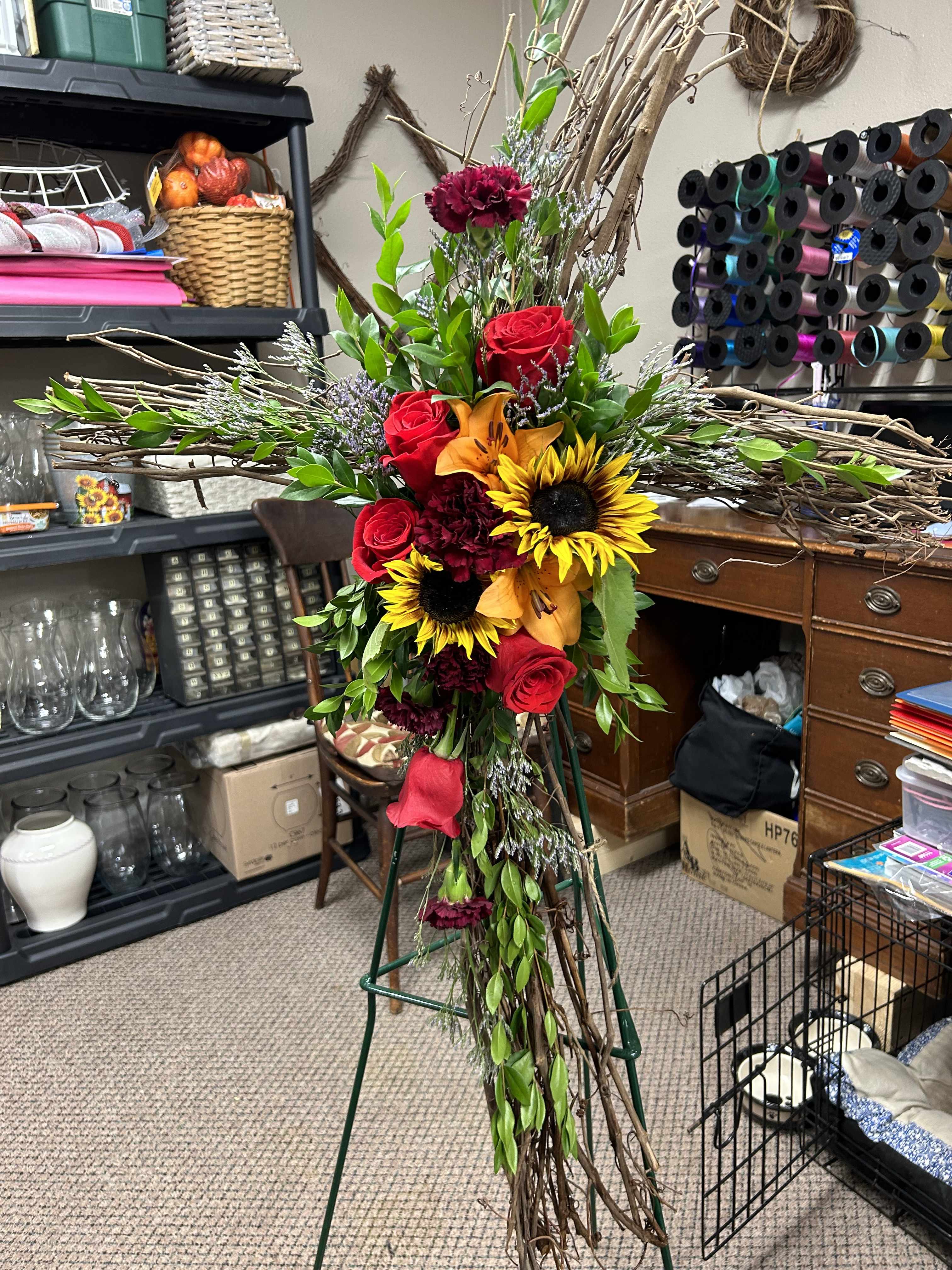 Tall floral cross with red roses, sunflowers, and orange lilies