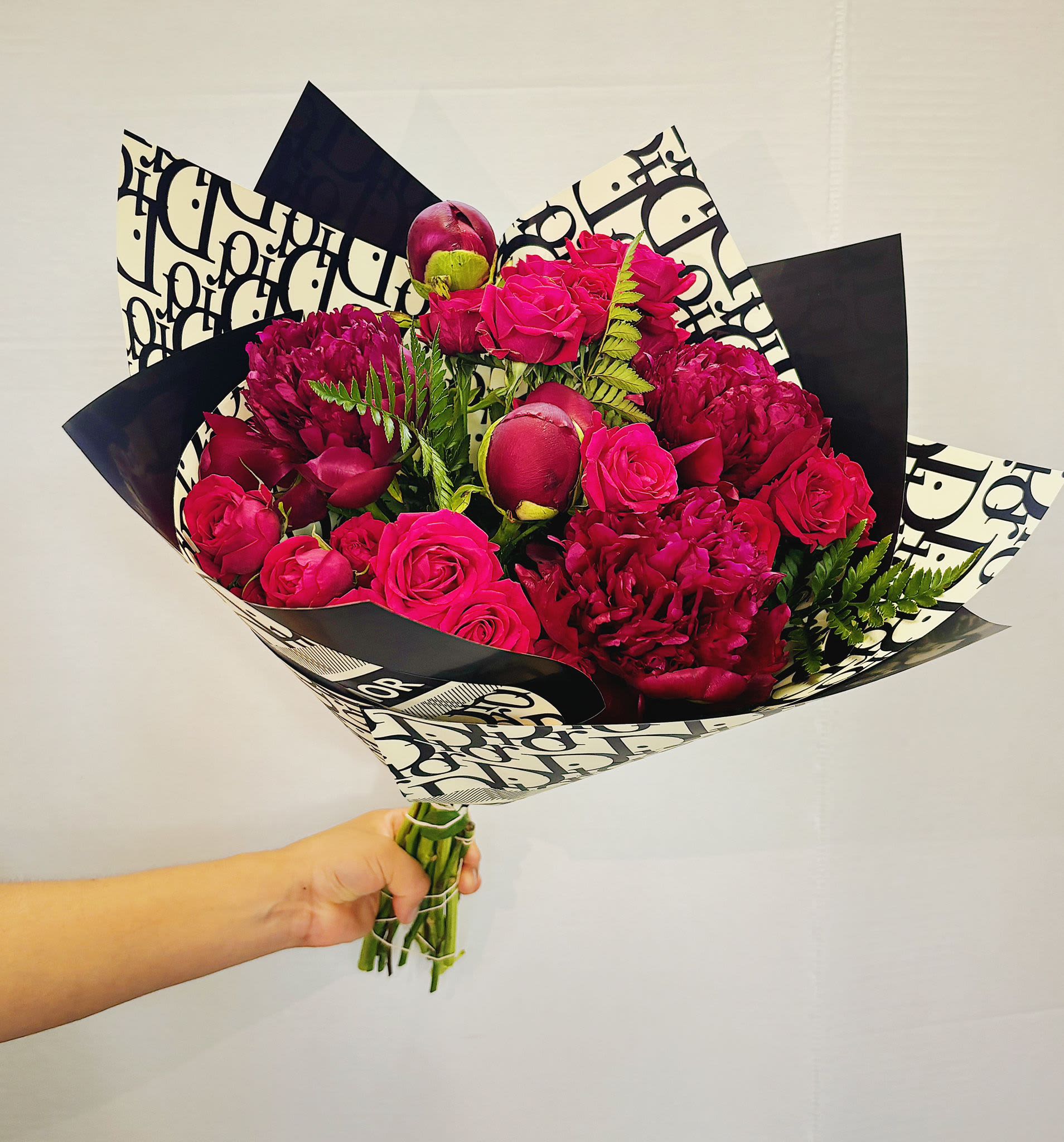 Handheld bouquet of hot pink roses and deep magenta blooms wrapped in black-and-white paper