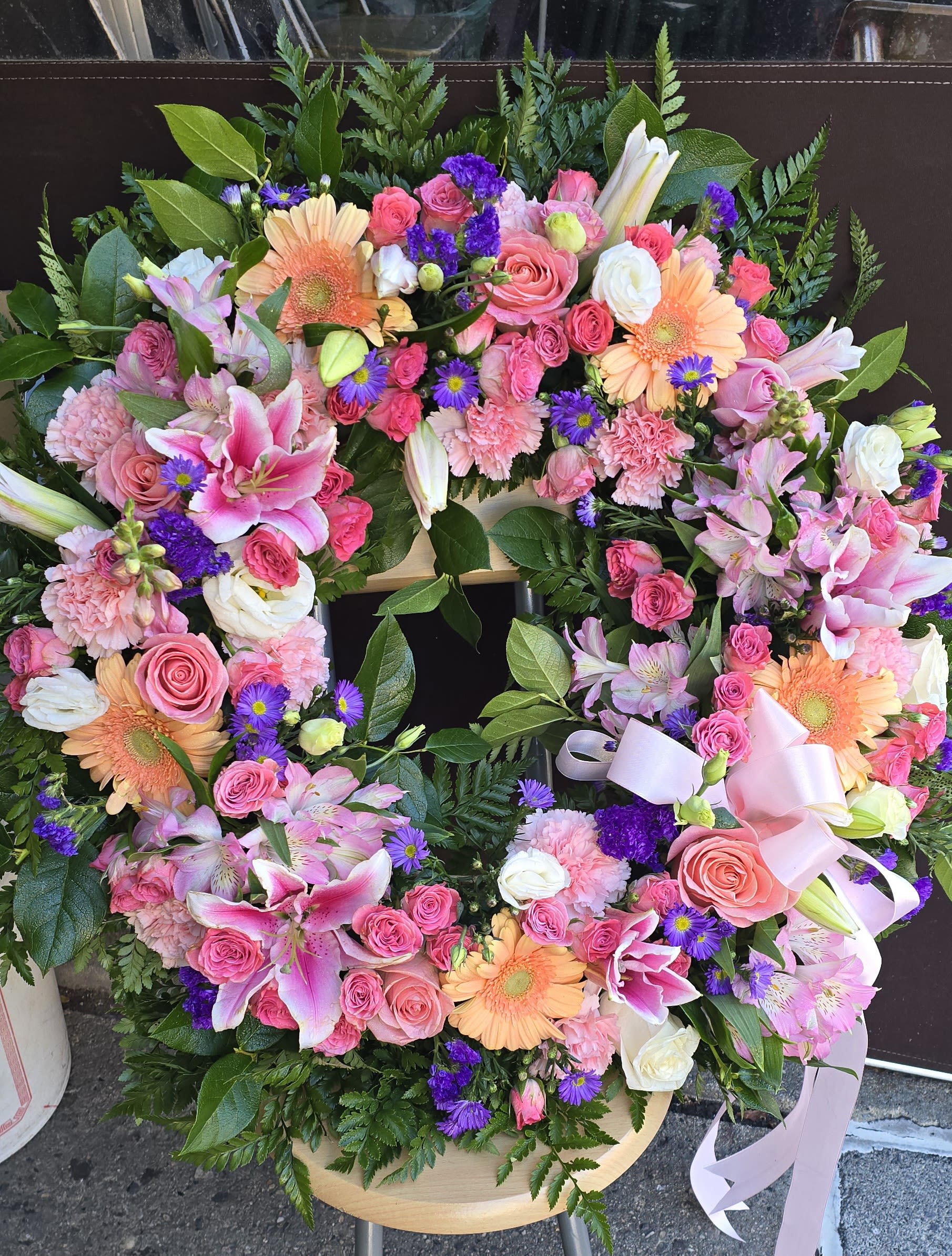 Infinity Love - Family and friends will recollect how special their loved one was with this gentle ring of pastel blooms. Highlighted with a pink satin ribbon, it is a lovely reminder of sweet memories and beautiful times shared. Peach roses, gerberas and carnations, pink asiatic lilies and lisianthus, along with purple limonium and lavender larkspur - accented by greens woven throughout - are presented on an easel-mounted wreath, ideal for a memorial occasion.