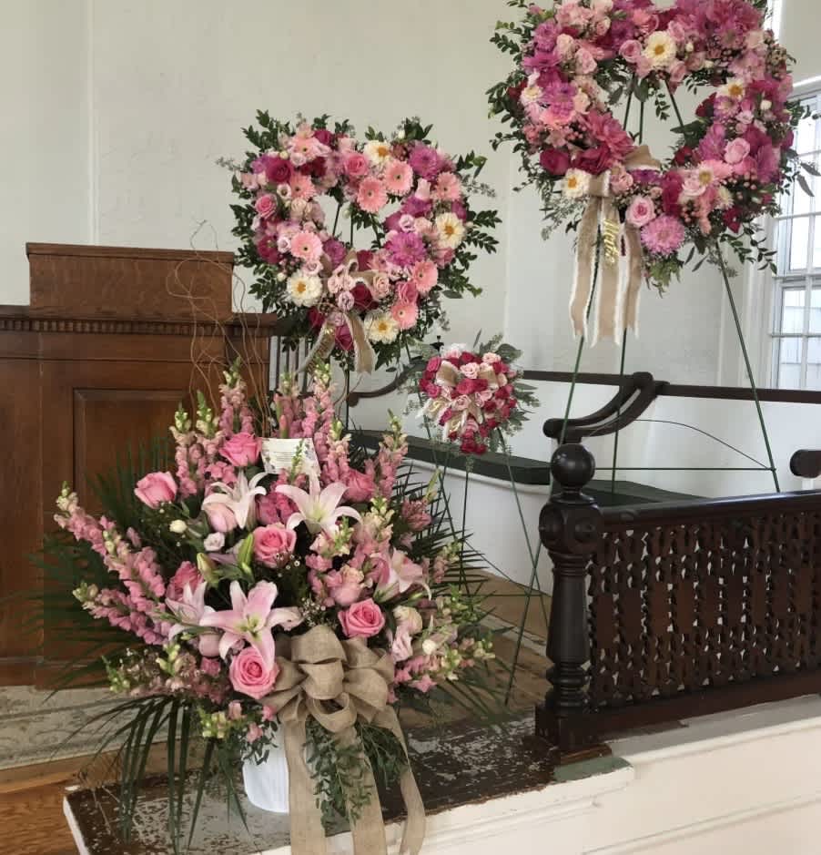 Pink floral wreaths and a large bouquet arrangement on stands in a church interior.