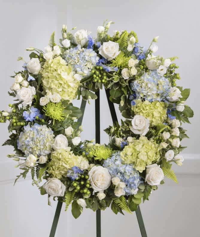 Floral wreath with white roses, blue hydrangeas, and pale green blooms on an easel