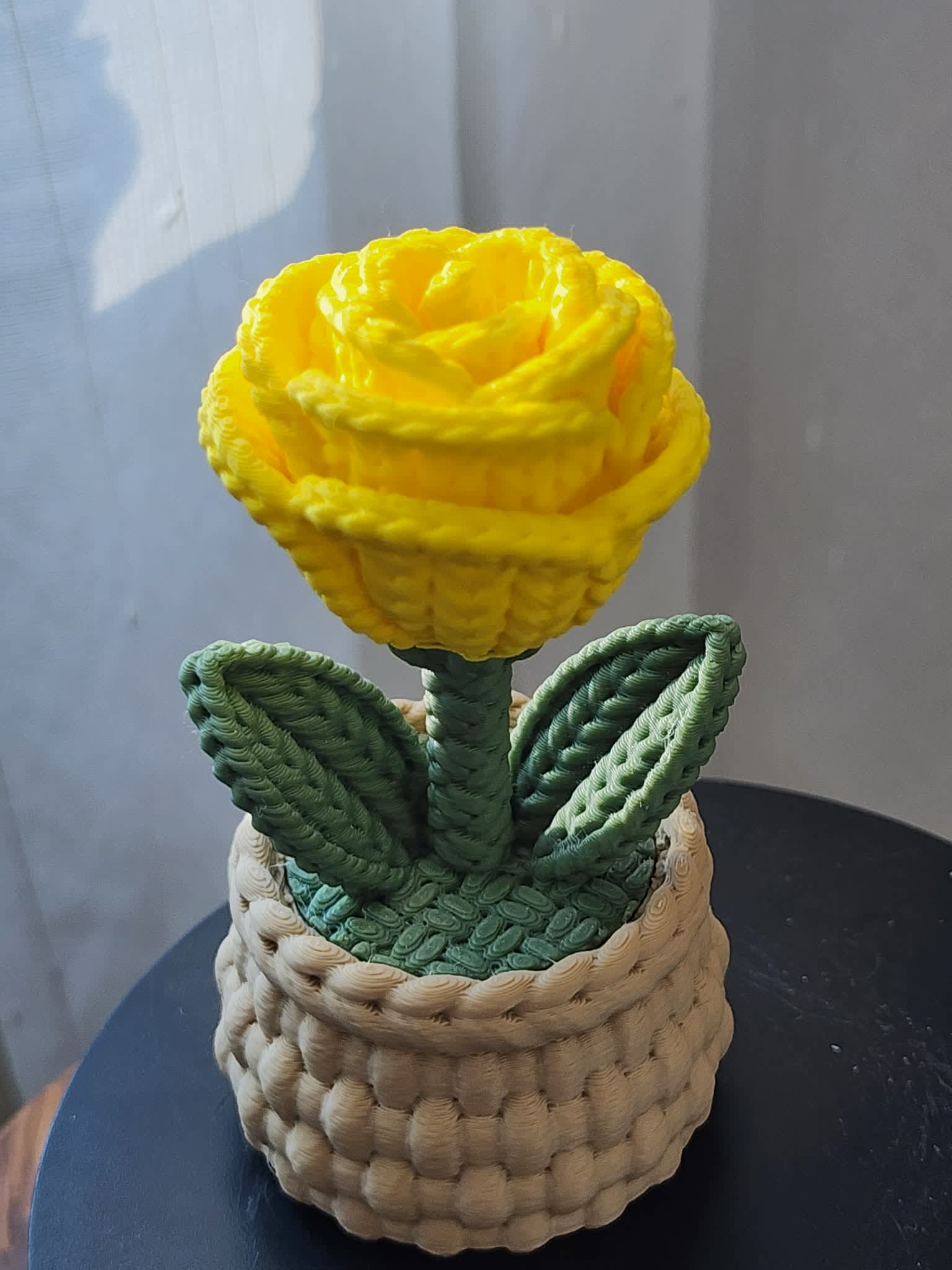 Yellow rose in a woven basket-style container with green leaves
