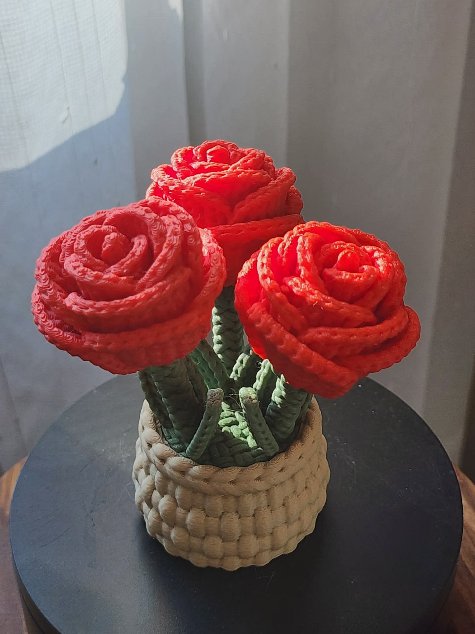Three red rose-shaped flowers in a woven basket container