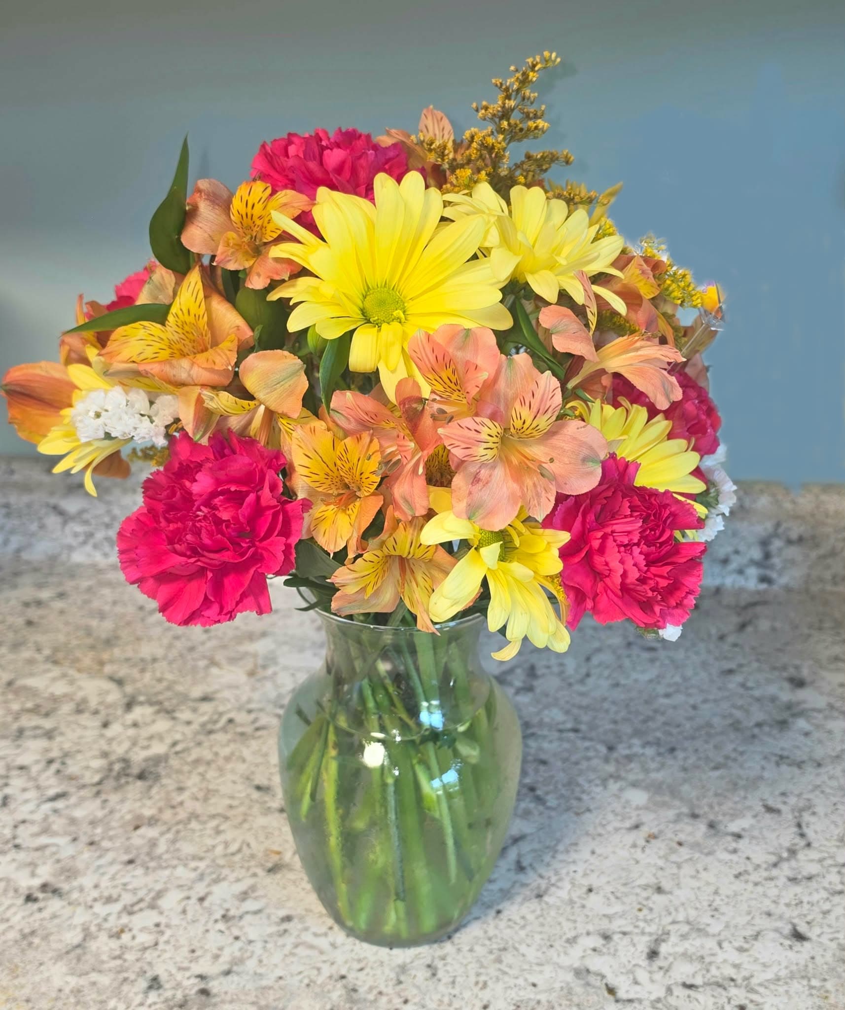 Mixed bouquet of yellow daisies, pink carnations, and peach alstroemeria in a glass vase