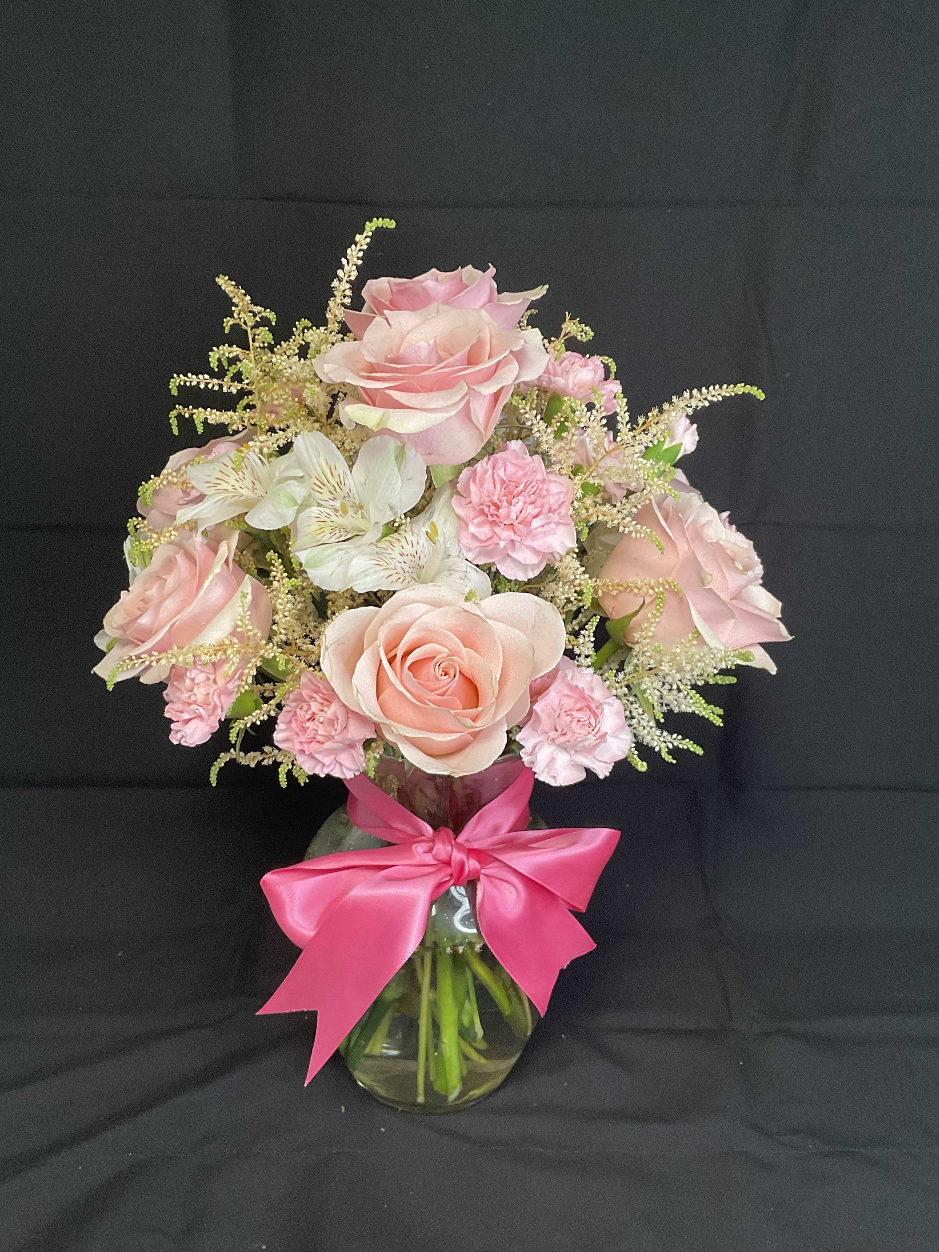 Pink roses and carnations in a glass vase with a bright pink bow