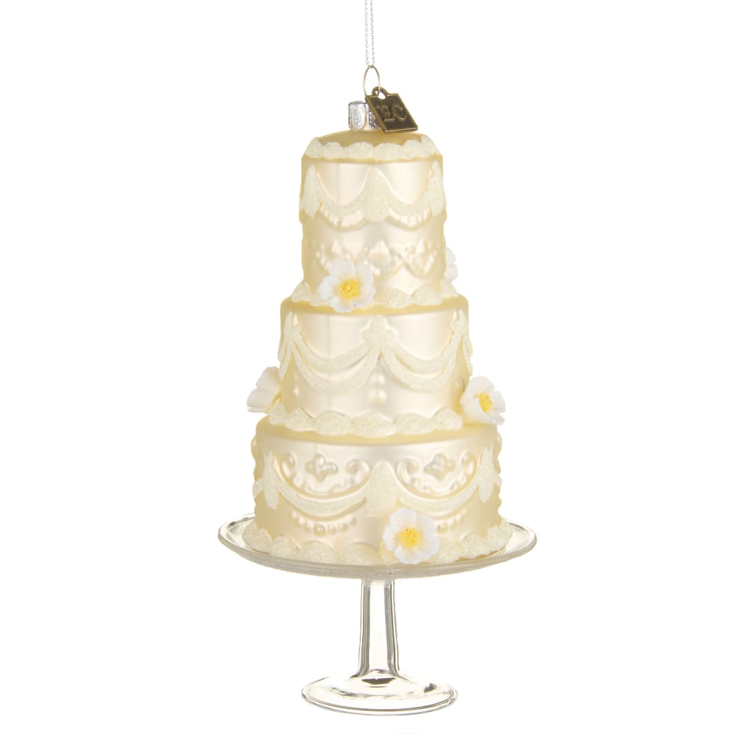 Three-tier ivory cake ornament on a glass stand with small white flowers