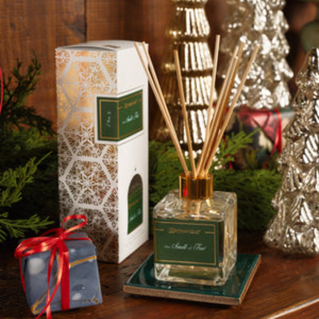 Reed diffuser bottle with boxed packaging and a small wrapped gift on a wooden surface