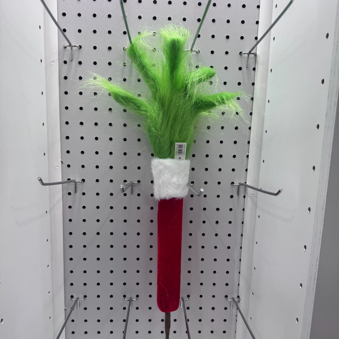 Green fuzzy decorative pick with a red handle hanging on a pegboard