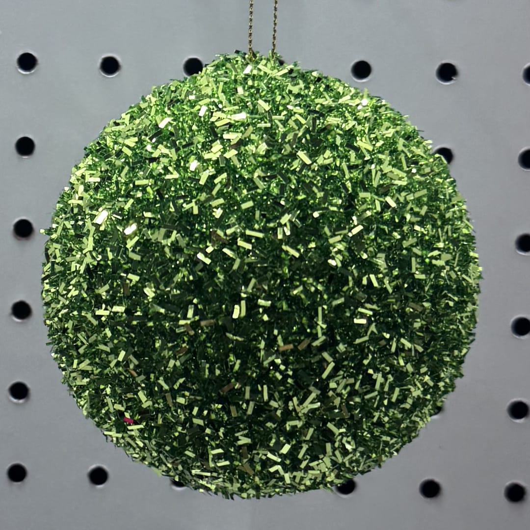 Green glitter ornament hanging against a perforated display board
