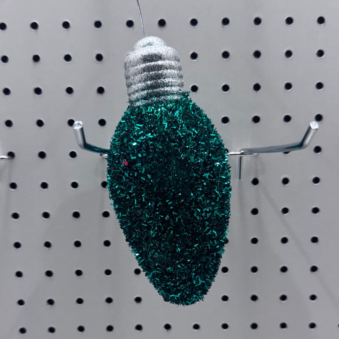 Teal glitter Christmas light ornament hanging on a pegboard