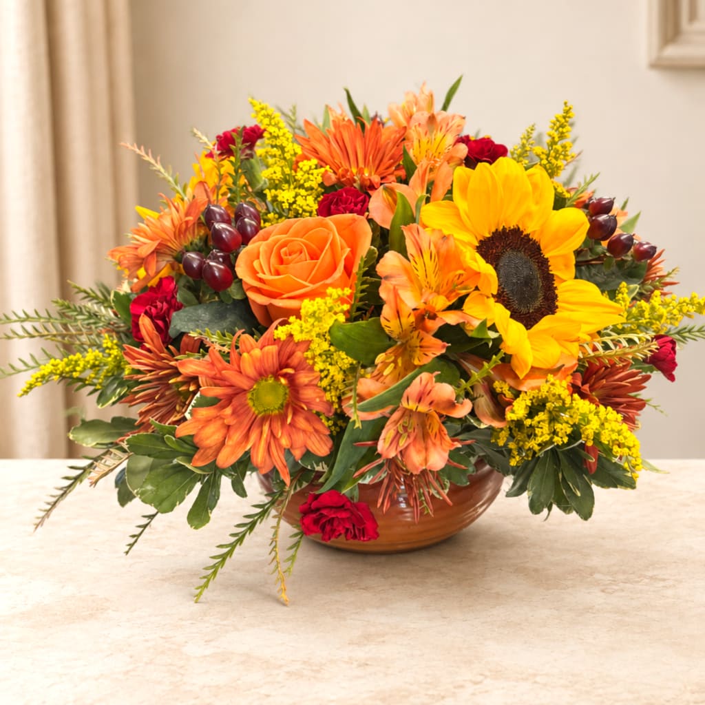 Bright mixed bouquet with sunflowers, orange roses, and red accents in a low bowl vase