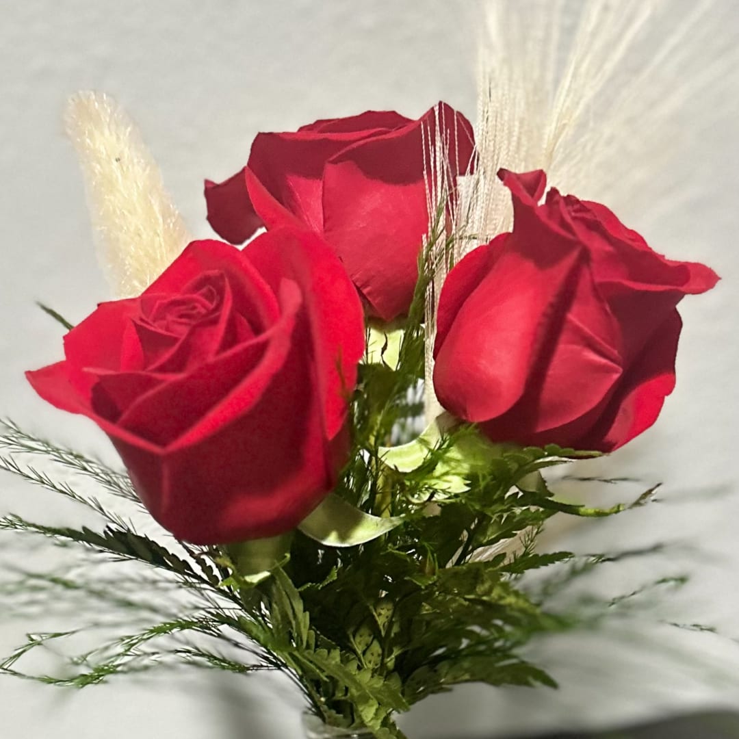 Three red roses with greenery and feathery accents