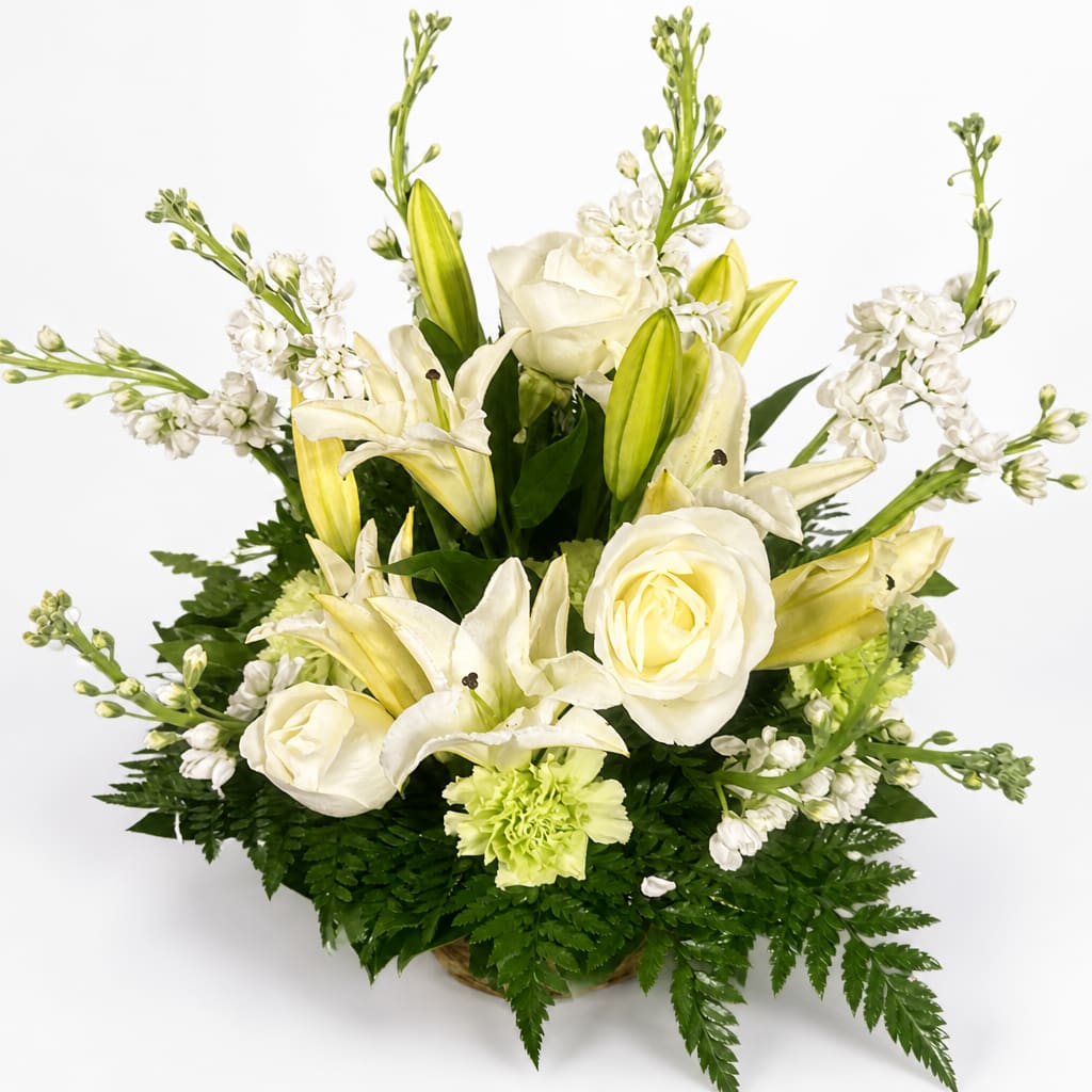 White roses and lilies arranged in a low basket with white filler flowers